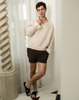 Man wearing a cream sweater and black shorts standing in a room with decorative elements.
