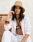 Woman wearing a straw hat, white shirt, and black bikini sitting on a wooden bench.