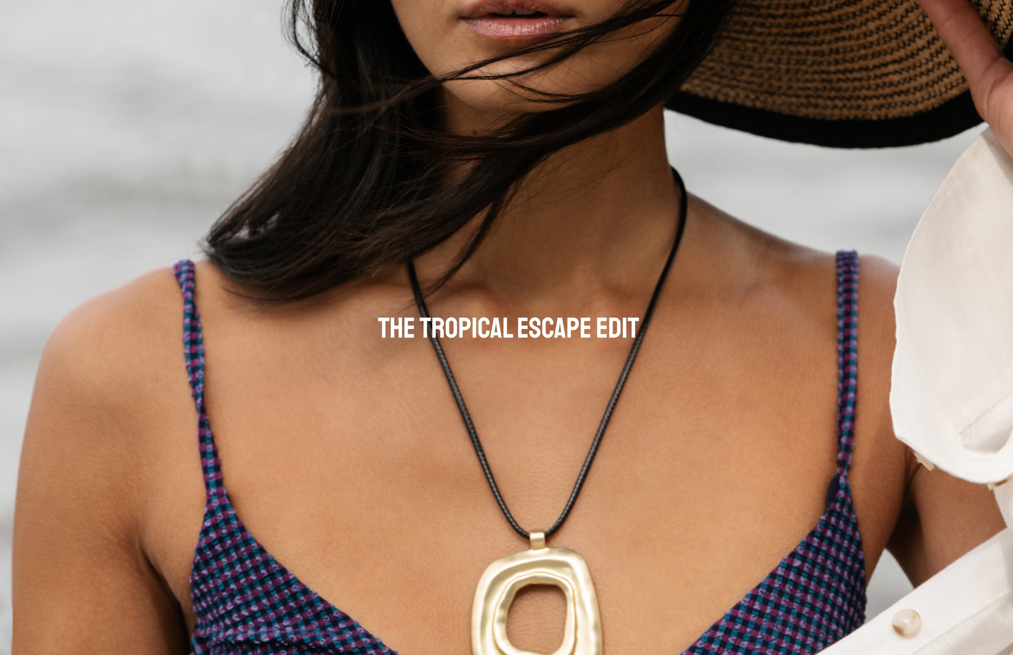 Woman wearing a gold necklace with 'The Tropical Escape Edit' text overlay.