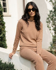 Woman in a beige outfit sitting outdoors with greenery in the background