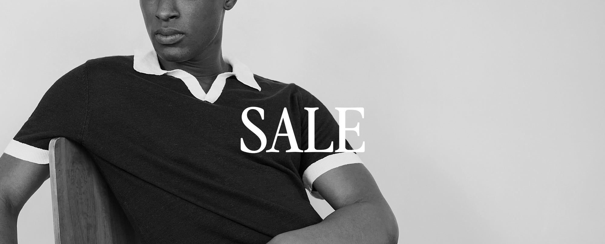 Person wearing a black polo with 'SALE' text, sitting on a chair against a plain background